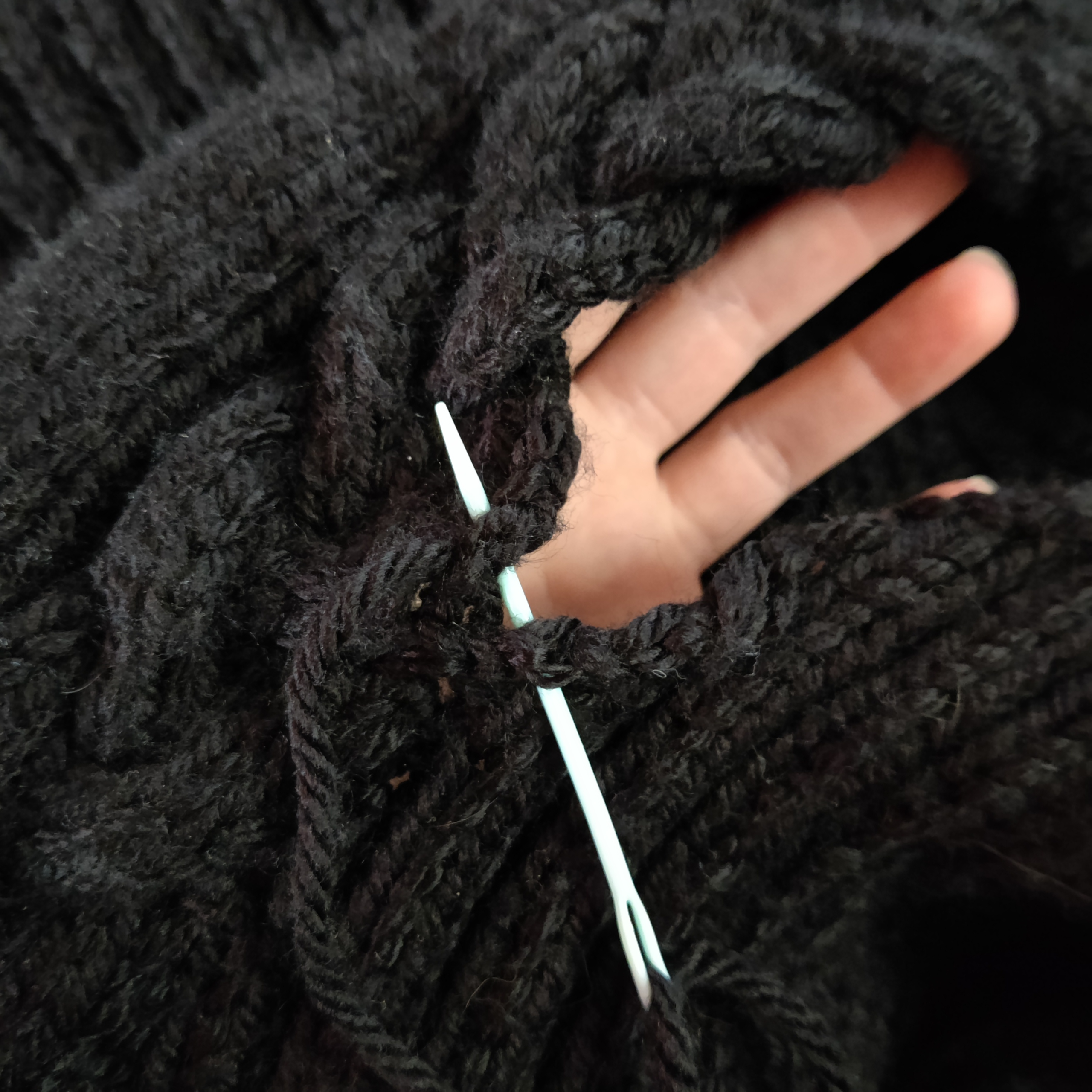 There's an end in sight for the Hopsmere sweater pattern! Image of a tapestry needle joining two panels of knitting, with a hand visible behind the open part of the seam.